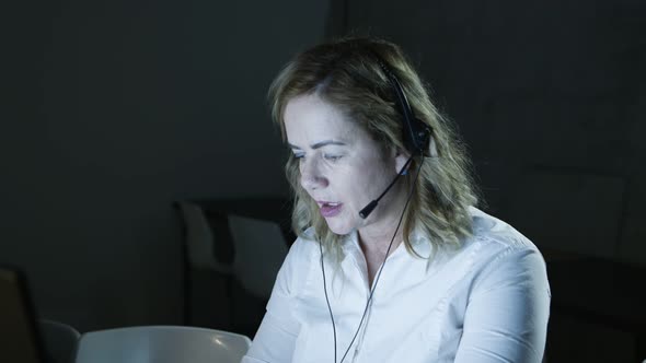 Serious Woman in Headset Working in Dark Office