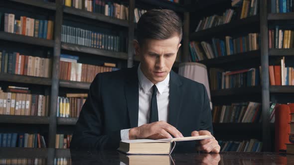 Businessman in Classical Suit Sitting in Library Reading Book