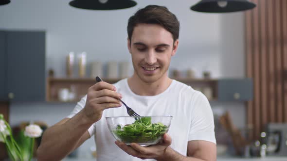 Smiling Man Eating Fresh Salad at Home Kitchen. Sporty Guy Enjoying Healthy Food