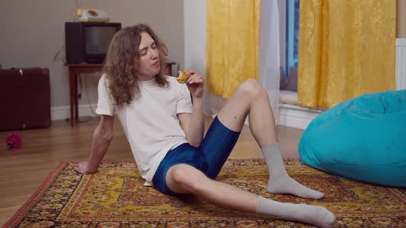 Relaxed Young Man Enjoying Sweet Tasty Donut After Training in Retro 80s or 90s Home