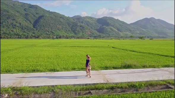 Drone Moves Over Woman with Girl Going Down Road Among Field