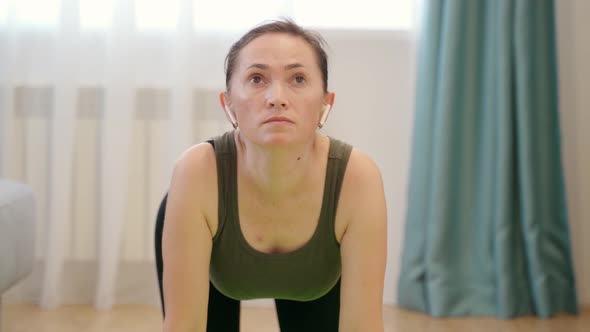 A Woman in a Tshirt Black Leggings is Doing Exercises on a Rug in a Bright Room