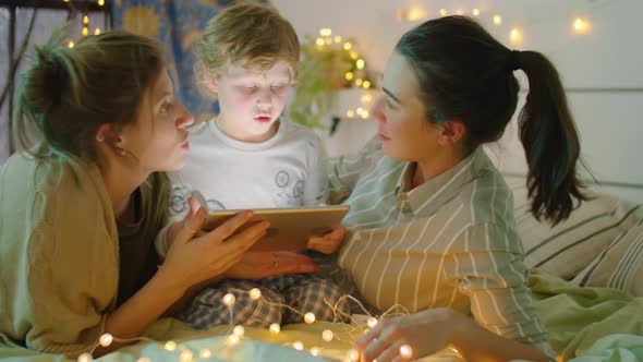 LGBTQ Family Using Tablet and Speaking on Bed with Garland