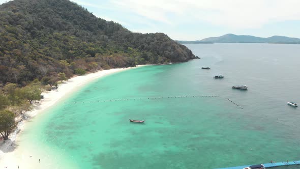 Lush Green hill and sandy shoreline encircling shallow turquoise sea of Koh Hey, Thailand