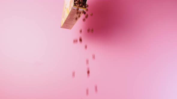 Chocolate Balls Made of Corn Flakes Fall Out of the Package on a Pink Background