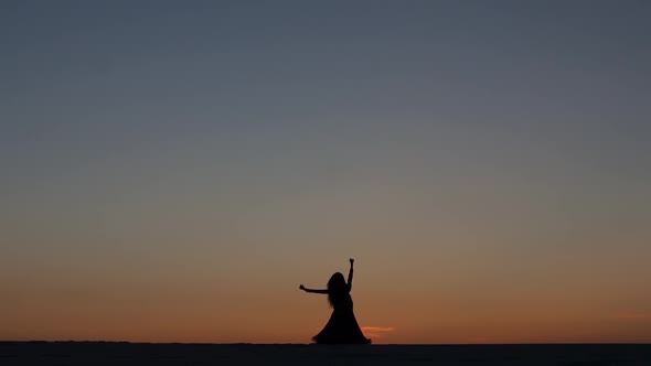 Dancer Sexually Dances on the Sand Against the Background of a Fiery Sunset. Silhouettes