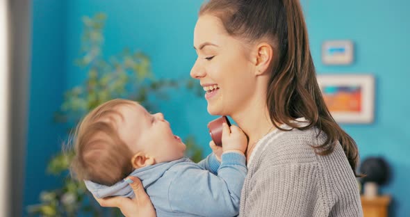 A Cheerful Smiling Women Spends Time in the Living Room Holding Baby in Arms Tilts