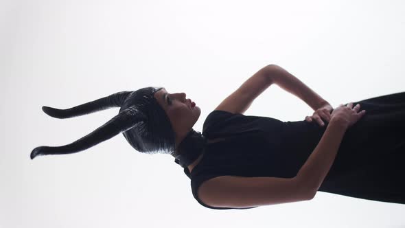 Attractive caucasian lady with horns in black clothing, posing with hands on her hips, looking into