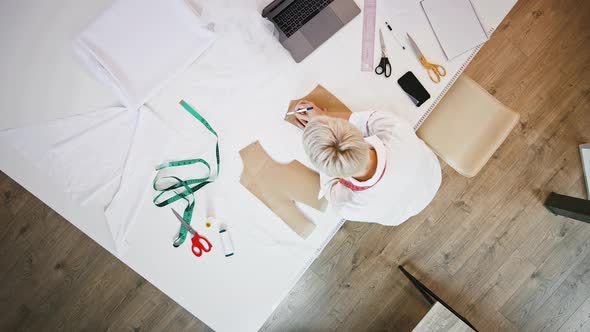 Female Tailor of Sewing Workshop is Drawing Pen Around Pattern Which Laying on White Fabric While