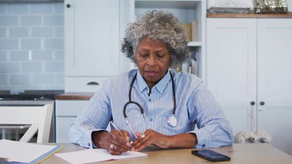 Portrait of senior african american female doctor talking notes while having a videocall at home