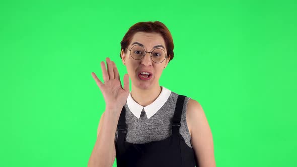 Portrait of Funny Girl in Round Glasses Is Waving Hand Hello, Flirting, Green Screen