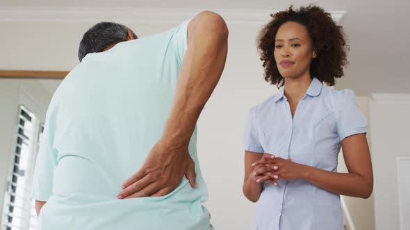 Mixed race female physiotherapist talking to senior man holding his back