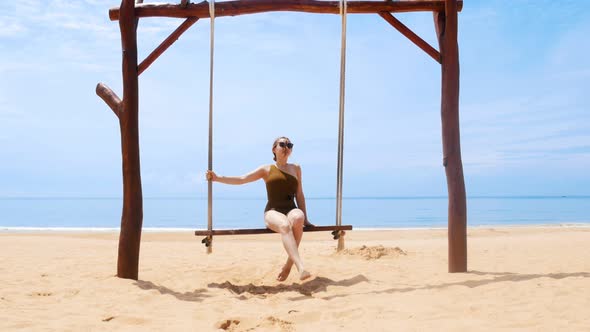 A Young Happy Woman Swinging on a Swings on the Beach