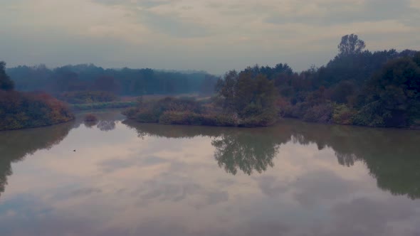 Backwards drone shot of a clear reflective lake in a forest on a beautiful autumn morning in the slo