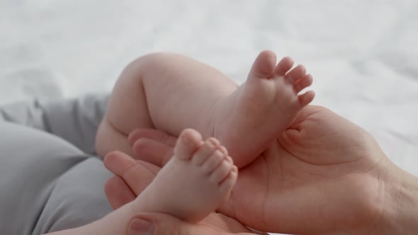 Loving Mom Playing With Tiny Legs Of Her Newborn Child At Home