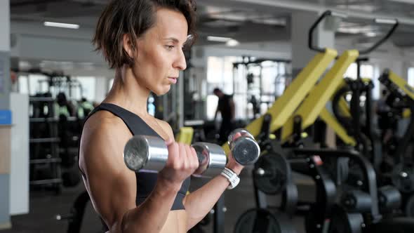 Sporty Mature Woman is Making Biceps Exercise with Dumbbells in Gym