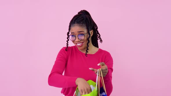 AfricanAmerican Girl in Pink Clothes Looks in Paper Laminated Bags with Handles and Shows the