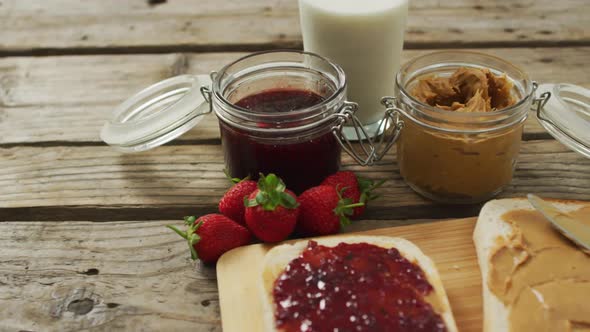 Peanut butter and jelly sandwich on wooden tray with milk and strawberries on wooden surface