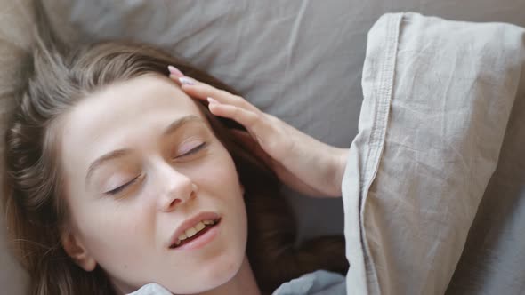 Young Woman with Long Hair Wakes Up, Gets Up on Bed and Stretches in Morning Sun Light