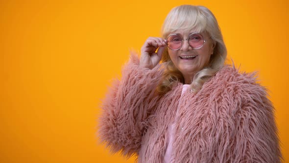 Positive Smiling Senior Lady in Pink Coat and Round Sunglasses Winking, Flirt