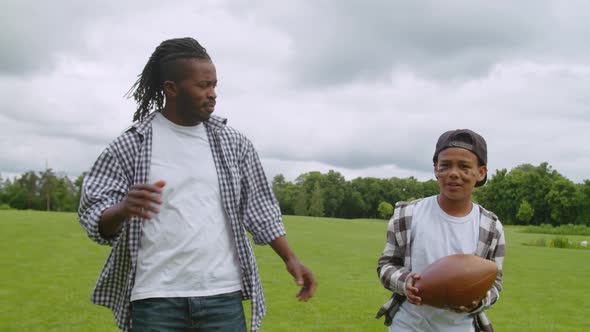 Happy African Dad and School Boy Walking on Field to Play American Football