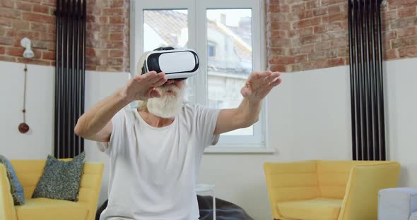 70-Aged Bearded Man in Home Clothes which Working on Virtual Screen in Augmented Reality Goggles