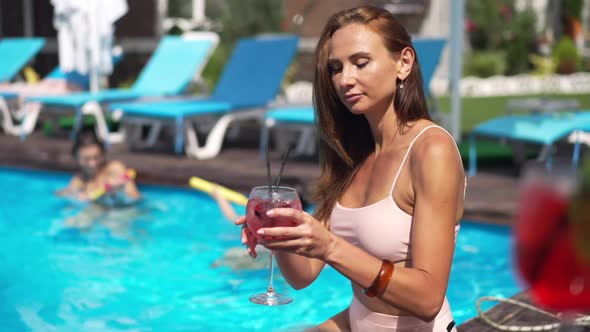 Portrait of Gorgeous Confident Caucasian Woman Drinking Cocktail at Poolside in Slow Motion
