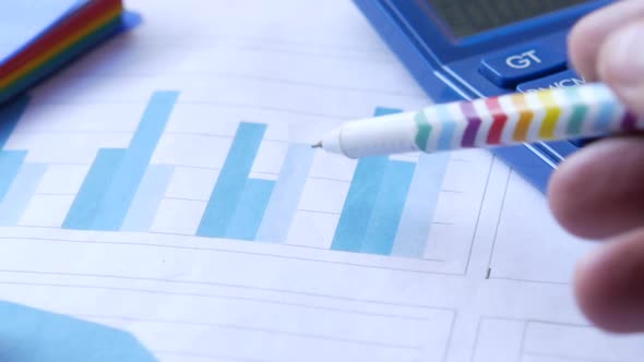 Man Hand with Pen Analyzing Bar Chart on Paper