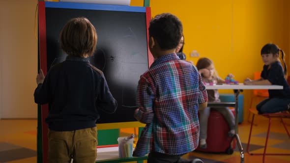 Diverse Boys Drawing at Blackboard in Kindergarten