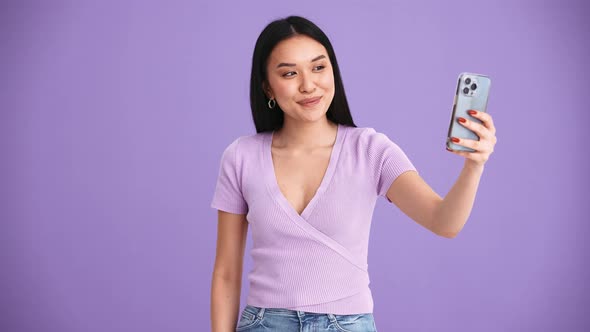 Smiling Asian brunette woman wearing purple t-shirt taking selfie photo by mobile