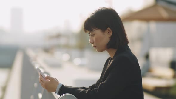 Asian Businesswoman Using Mobile Phone on Urban Embankment
