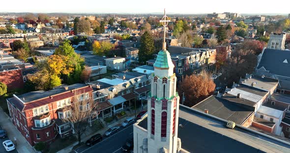 Aerial orbit of Christian church with steeple and cross, crucifix. Fall foliage during golden hour.