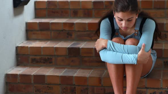 Sad schoolgirl sitting alone on staircase