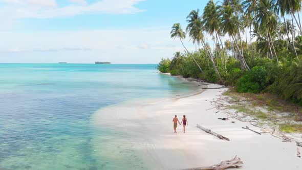 Aerial slow motion: couple walking on tropical beach at sunset, away from it all