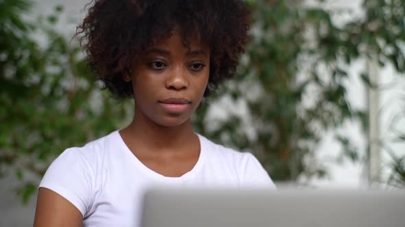 Closeup Face of Focused African Young Woman Working Typing on Laptop Computer Sitting at Desk in