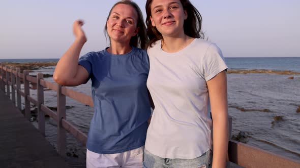 Mother and daughter standing on sidewalk by the sea at sunset