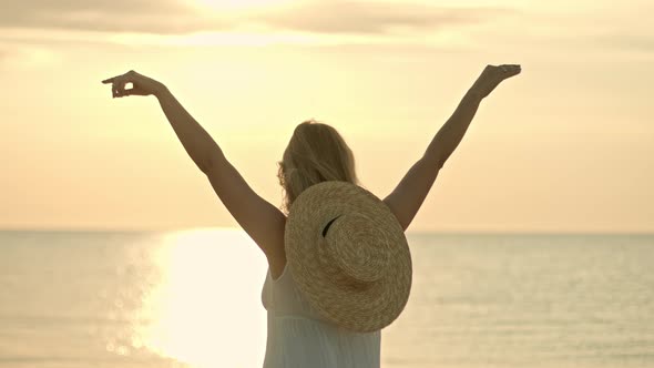 Woman in White Dress and Straw Hat Standing with Open Arms on Sea Beach. Beauty, Nature, Travel