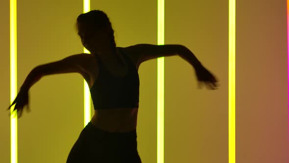 A Girl Performs Freestyle Dances Indoors Against a Background of Multicolored Neon Tubes Enjoying