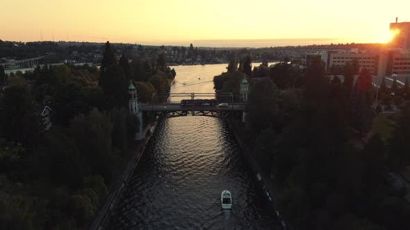 City Waterway Aerial Following Boat To Historic Bridge With Cars Commuting At Sunset