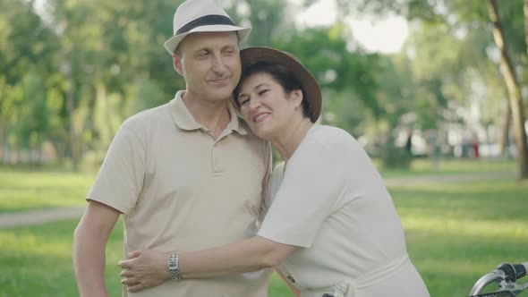 Happy Loving Woman Hugging Husband in Park and Smiling at Camera. Man Looking at Wife with Love