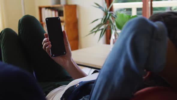 Caucasian woman using smartphone, lying on sofa at home