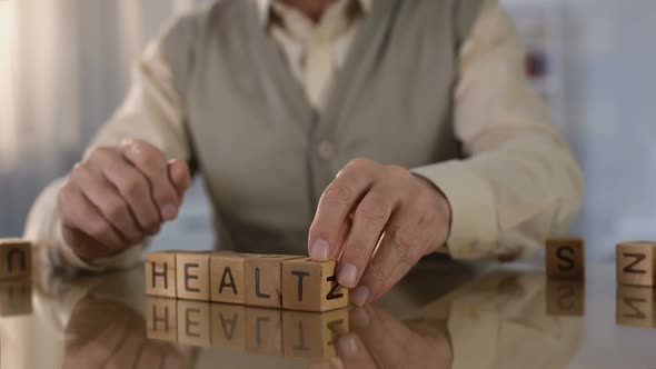 Grandfather Making Word Health of Wooden Cubes on Table, Elder Care, Medicine