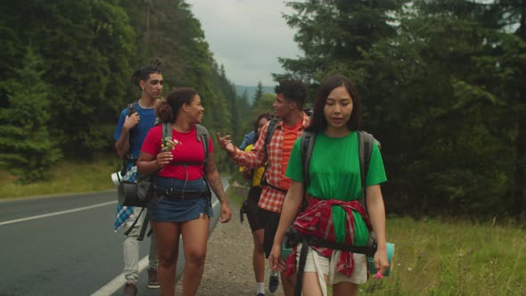 Joyful Diverse Multicultural Tourists with Backpacks Hiking Along Freeway in Mountains