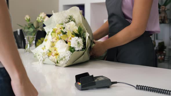 Man Buys Bouquet in Flower Shop Pays By Card in Payment Terminal Hands Closeup