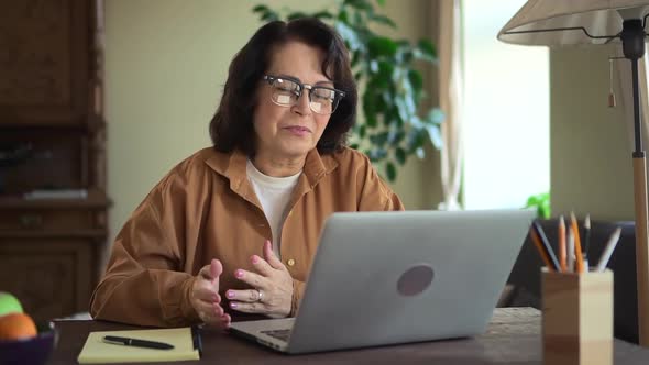 Woman Having Online Talk and Sitting at Table with Laptop in Home Room