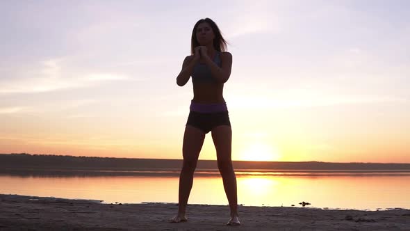 Young Attractive Woman Doing Sport Exercises in the Morning on Sunrise Beach By Sea or Lake