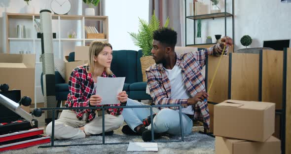 Couple Sitting on the Carpet in their New House and Measuring dimentions