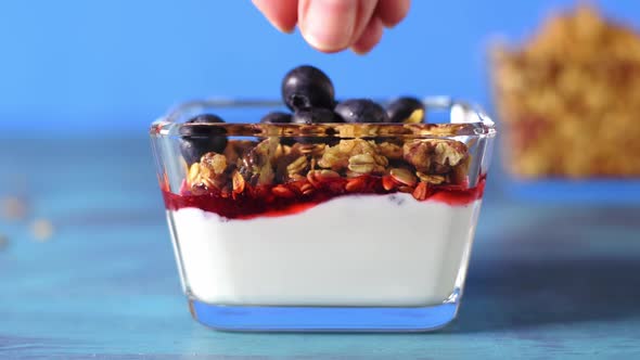 Adding blueberry to yogurt, granola and jam. Healthy breakfast