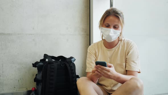 Woman Using Mobile Phone at the Airport in the Waiting Room While Wearing Face Mask Due to Covid19