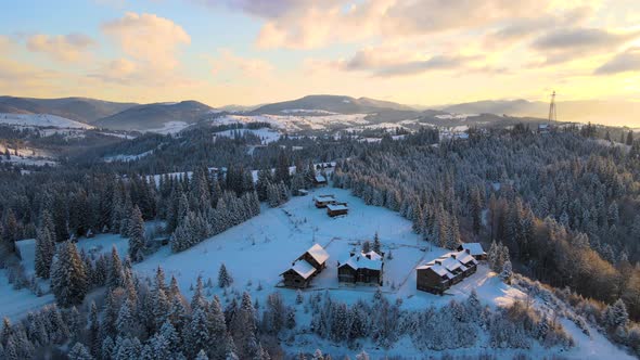 Aerial winter landscape with small village houses between snow covered forest in cold alt